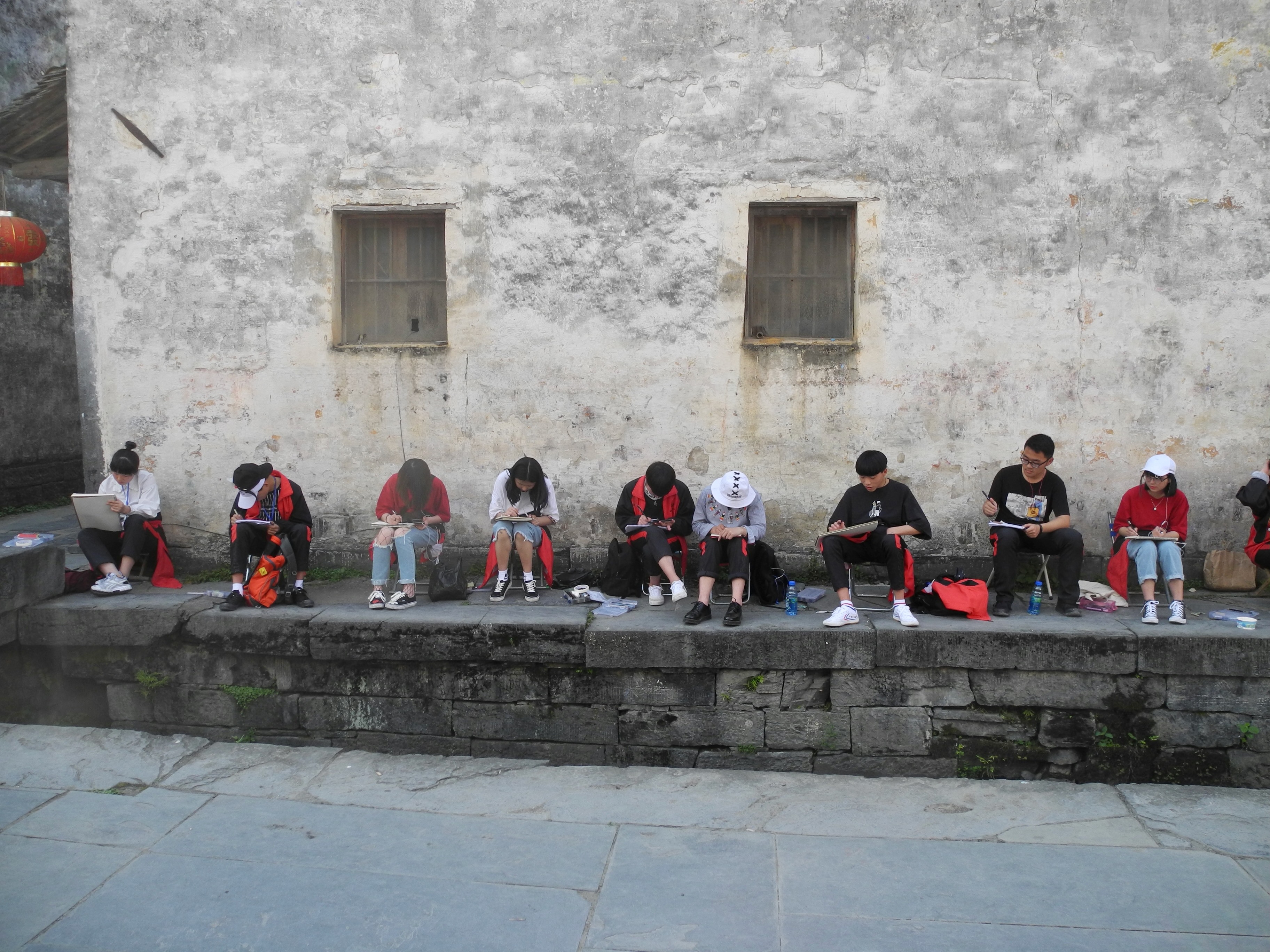 Jeunes étudiants en art dessinant le long d'un mur ancien dans un village de l'Anhui