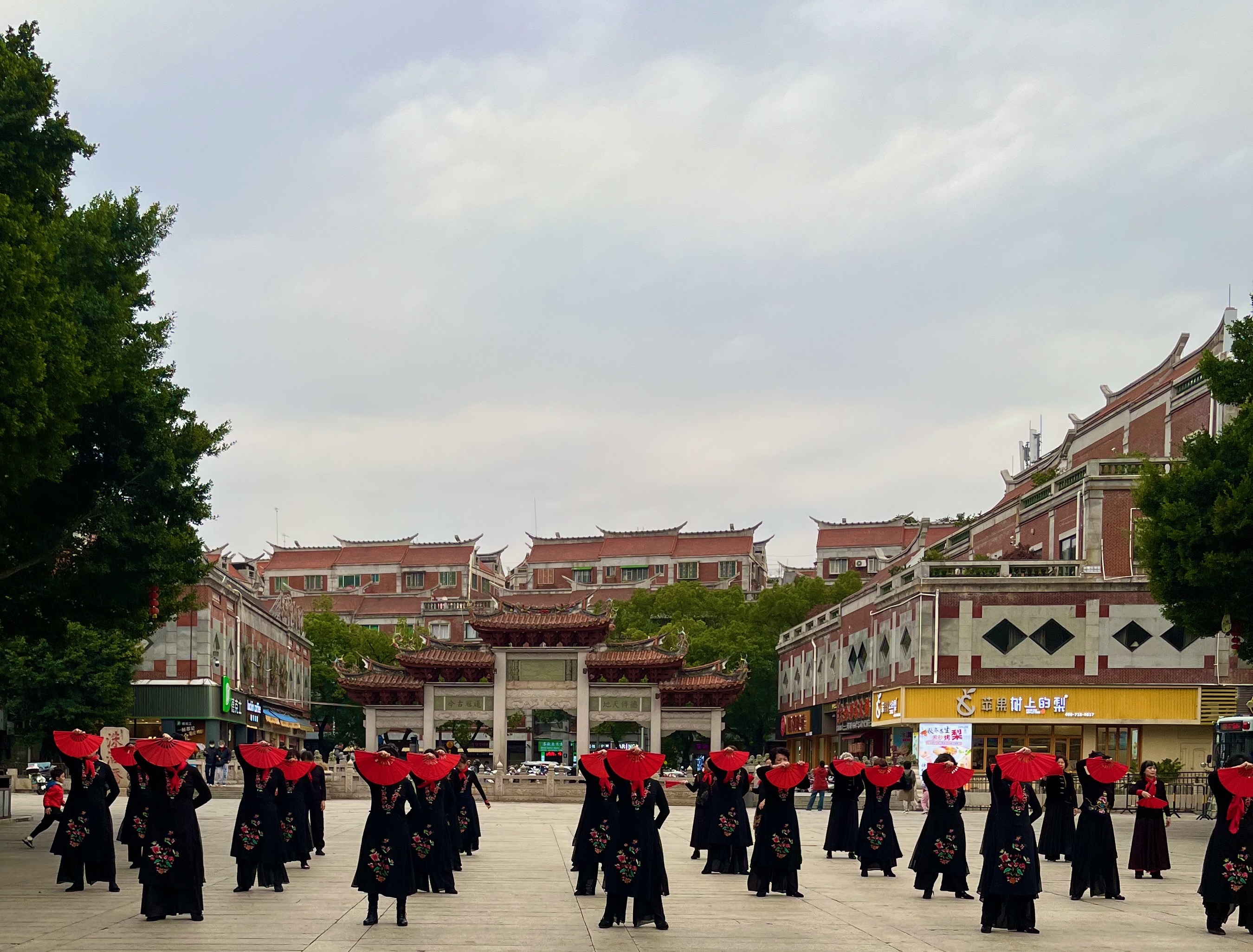 Danseuses aux éventails rouges sur une place de Quanzhou, devant un portique traditionnel